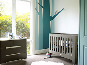 blue_tree_feature_wall_nursery_grey_cot_carpet_fluffy_white_rug_dark_grey_drawers_monkey_toy